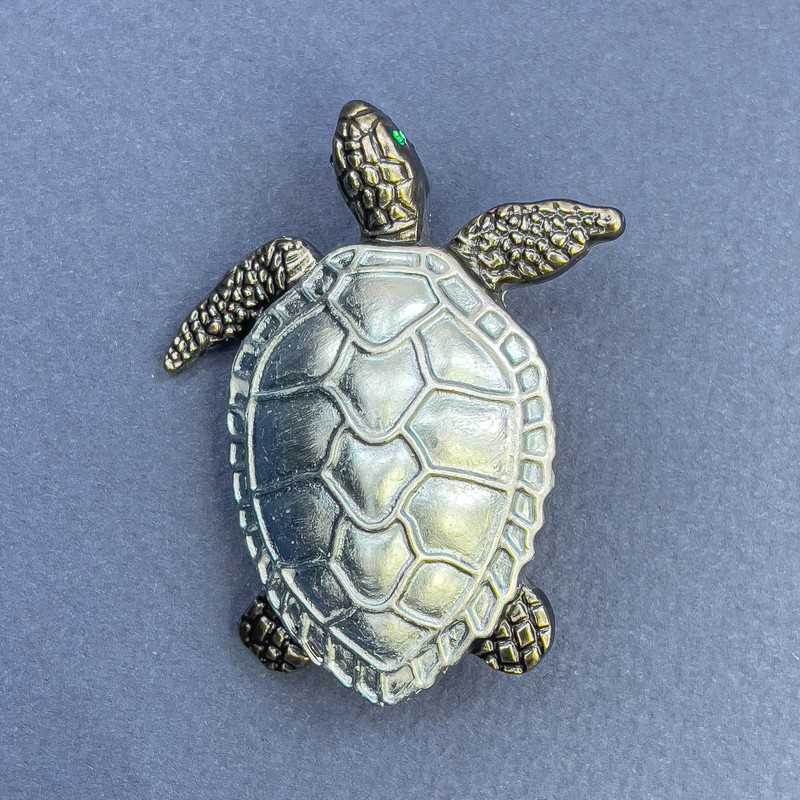 סיכת-תליון צב בצבע כחול-אפור ומתכת כסופה, קוטר 40 מ״מ, אורך 49 מ״מ